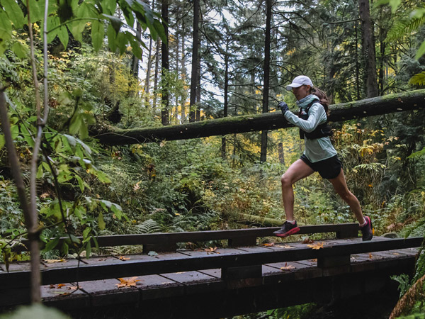 Trail runner crossing trail bridge wearing Cloudline socks