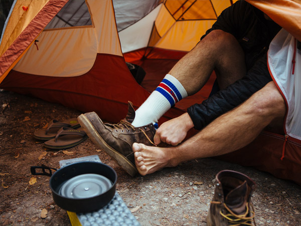 backpacker sitting in tent putting on Cloudline socks and hiking boots