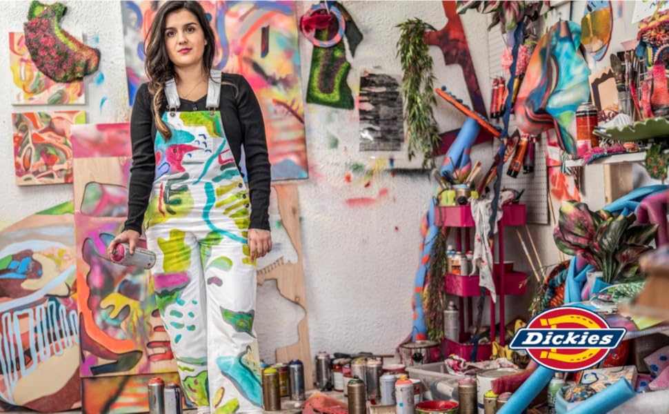 artist in white painted overalls holding spray paint can in colorful studio