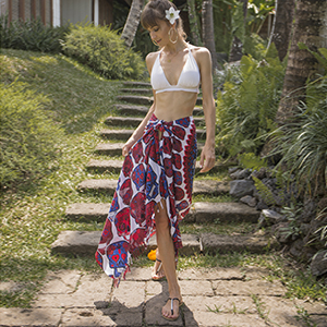 Woman wears blue/red and pink sugar skull sarong styled as skirt near plants and stone stairs