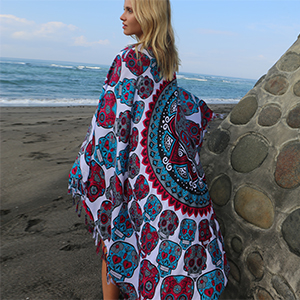 Woman wears blue/red and grey sugar skull sarong styled as shawl/blanket near ocean